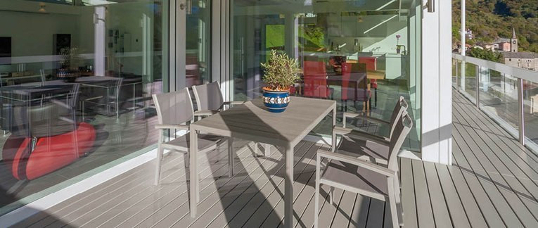 Überdachte Terrasse mit grauem Holzboden, modernem Esstisch-Set und Blick in den offenen Wohnbereich.