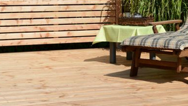 Holzterrasse aus Lärche mit Liegestuhl, kariertem Polster, kleinem Tisch mit grüner Tischdecke und Sichtschutz aus Holzlatten.